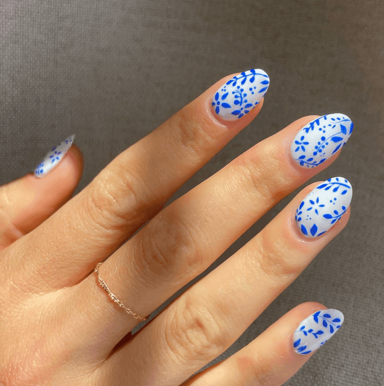 Hand with blue floral nail art on a white background, wearing a thin gold ring.