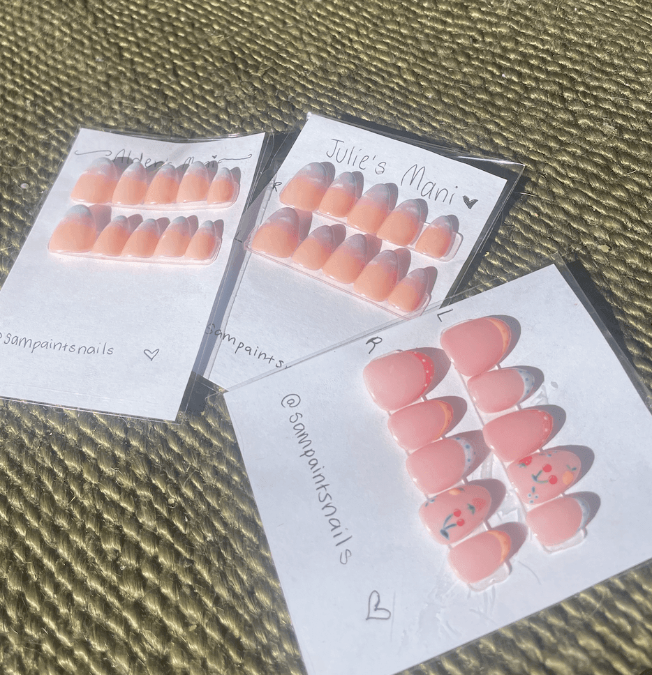 Three sets of decorative nail tips on cards with designs and inscriptions.