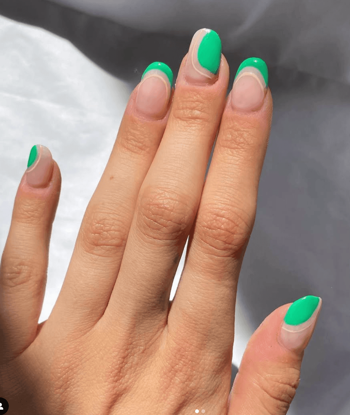 Hand with bright green French manicure against a soft background.